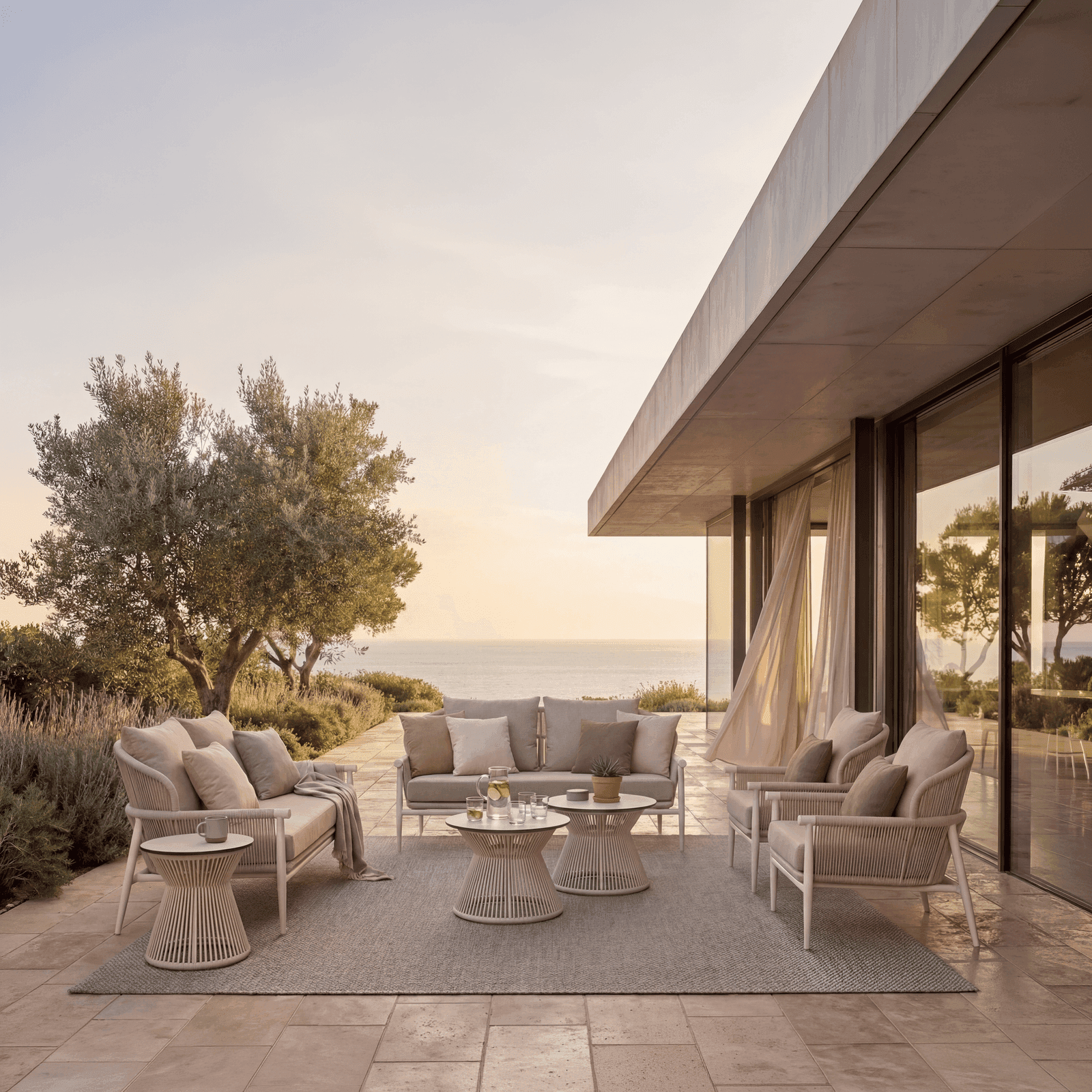 Outdoor lounge set with light woven sofas, armchairs, and slatted coffee tables on a tiled Mediterranean coastal terrace at.