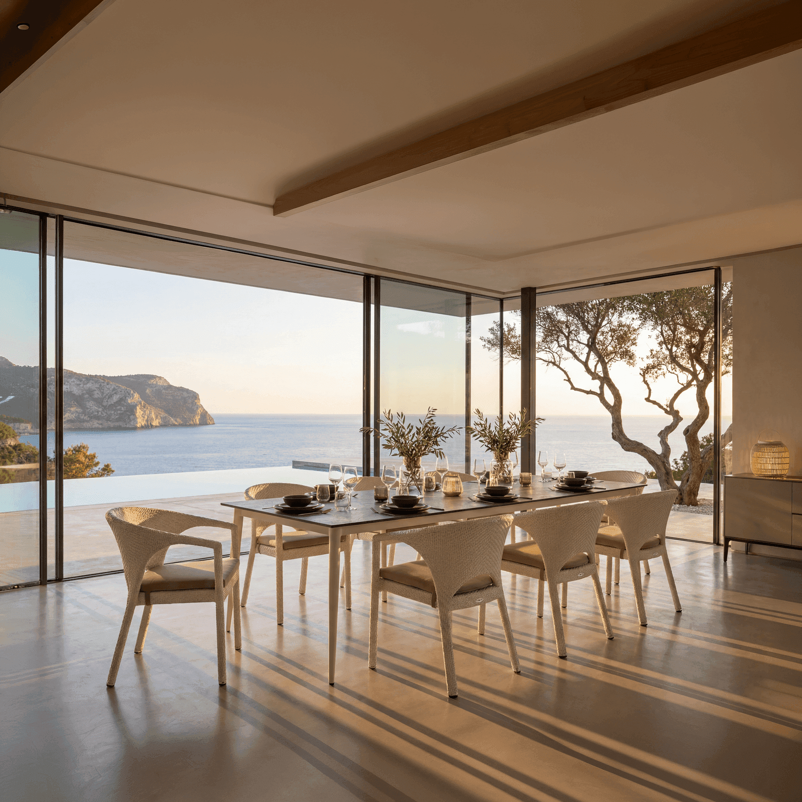 Ivy outdoor dining set with woven chairs and a dark-top table, placed in a modern villa overlooking a Mediterranean coast.