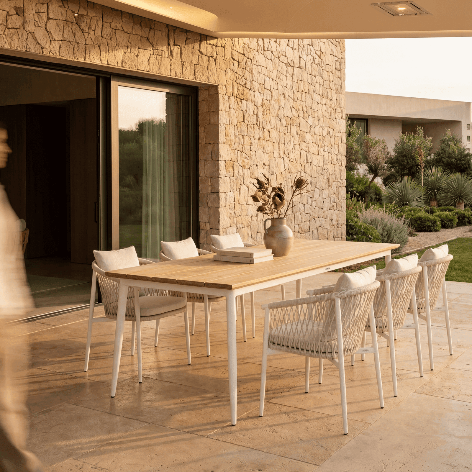 Air collection outdoor dining set with teak table, white aluminum frame, and woven rope chairs with cushions on a.